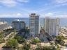 Aerial perspective of coastal high-rise properties featuring direct ocean frontage, structured surface parking, and mature palm landscaping