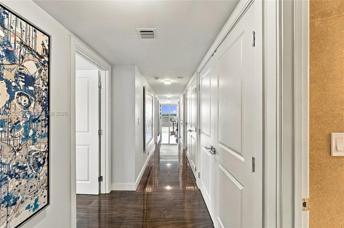 Hallway featuring dark wood-finish flooring, crisp white walls, and multiple solid-core interior doors with satin nickel hardware
