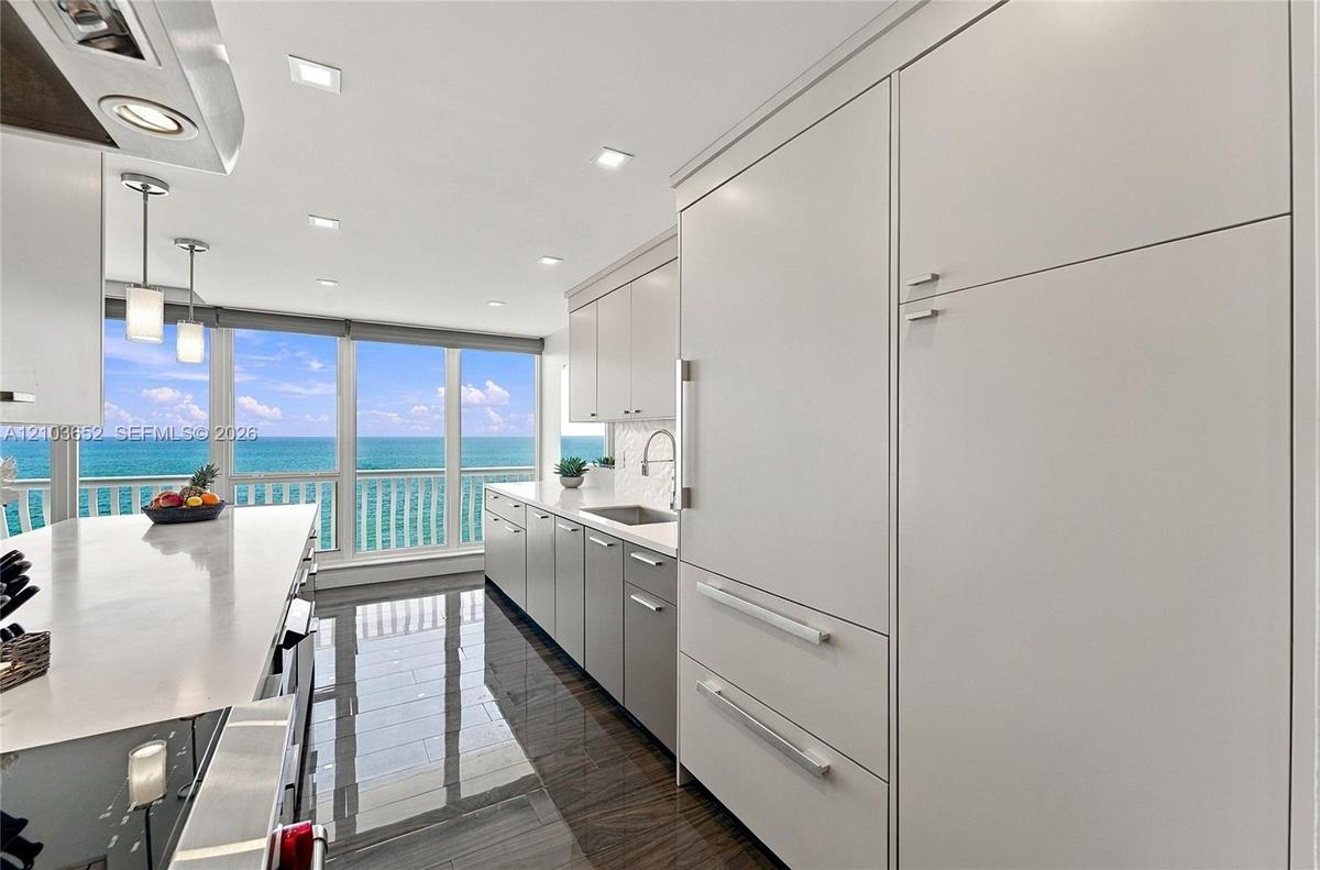 Kitchen featuring high-gloss cabinetry, stone countertops, integrated refrigerator, recessed lighting, and expansive windows with water backdrop