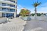 Expansive paved terrace featuring a custom outdoor kitchen with tiled base, metal pergola, and perimeter glass balcony railings