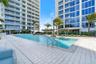 Expansive outdoor swimming pool featuring stainless steel handrails, light-toned stone decking, mature palm trees, and structural shade pavilions