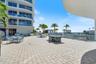 Expansive paved terrace featuring a tiled outdoor kitchen island, glass-panel perimeter railing, and mature palm landscaping