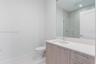 Bathroom featuring a vanity with wood-finish cabinetry, light-toned countertop, undermount sink, large wall-mounted mirror, and glass-enclosed shower