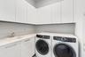 Laundry area featuring high-gloss white upper and lower cabinetry, solid surface countertop, and an integrated basin with a chrome faucet