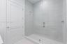 Walk-in shower featuring large-format porcelain tile surround, frameless glass enclosure, polished chrome fixtures, and built-in tiled bench