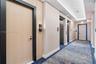 Elevator lobby featuring wood-panel doors with black trim, stainless steel elevator banks, recessed ceiling lighting, and patterned carpeting