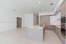 Kitchen featuring wood-finish cabinetry, white high-gloss upper cabinets, solid-surface countertops, large kitchen island with integrated sink, and bu
