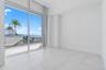 Floor-to-ceiling glass wall, large-format tile flooring, and sliding glass door opening to a private balcony with glass railing and water backdrop