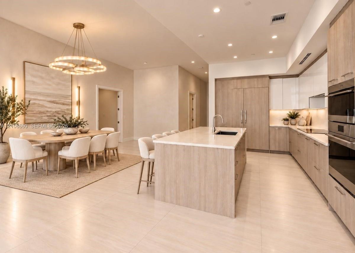 Kitchen featuring light wood-finish cabinetry, a large central island with light-toned countertops, integrated stainless steel appliances, recessed li