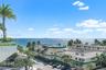 Oceanfront setting featuring a glass-panel balcony railing, mature palm trees, and expansive coastal exposure