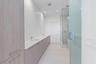 Dual-sink vanity with wood-finish cabinetry, light stone countertop, walk-in glass-enclosed shower, and tile flooring