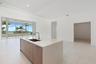 Kitchen island featuring stone countertops, a stainless steel undermount sink, and wood-finish cabinetry, set against large floor-to-ceiling windows w