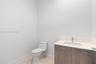 Bathroom featuring a wood-finish vanity with a stone-composite countertop, integrated rectangular sink, chrome-finish faucet, and a one-piece elongate