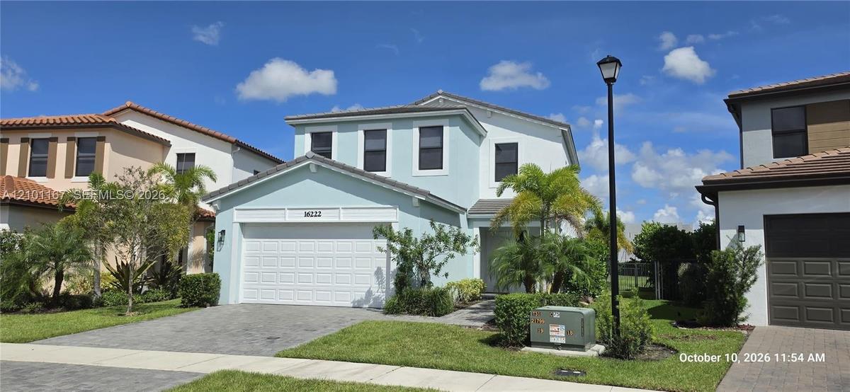 Two-story residence featuring a light-toned exterior, concrete tile roof, multi-panel garage door, and a paver driveway