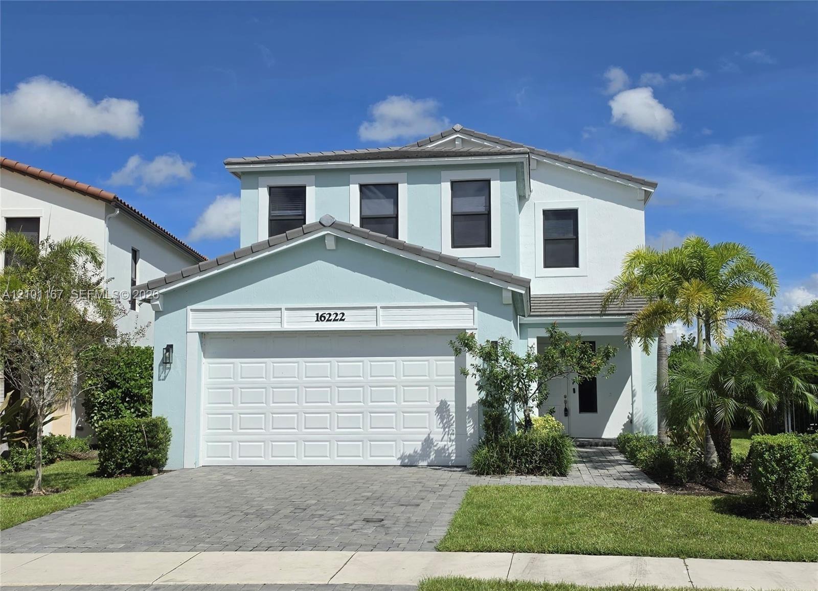 Two-story exterior featuring light-toned stucco, a multi-gabled roofline, an attached two-car garage, and decorative horizontal siding trim
