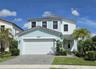 Two-story exterior featuring light-toned stucco, a multi-gabled roofline, an attached two-car garage, and decorative horizontal siding trim