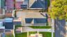 Aerial view featuring a multi-section roofline, expansive concrete hardscaping, a detached garage, and a fenced perimeter