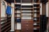 Custom walk-in closet featuring floor-to-ceiling wood-finish cabinetry, adjustable shelving, integrated hanging rods, and a three-drawer built-in dres