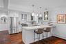 Kitchen featuring white cabinetry, stone countertops, stainless steel appliances, wood-finish flooring, and three glass pendant lights
