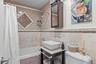 Bathroom featuring a vanity with a rectangular vessel sink, stone countertop, tiled tub surround with decorative mosaic inlay, and a wall-mounted medi