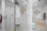Walk-in glass-enclosed shower featuring a stone-tile floor, built-in corner seat, rain-style showerhead, and decorative mosaic tile accent