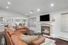 Vaulted ceilings with recessed lighting, dark wood-finish flooring, and a fireplace featuring a detailed mantel, tiled surround, and column accents