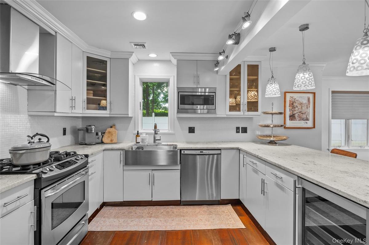 Kitchen featuring white cabinetry, light-toned stone countertops, stainless steel apron-front sink, wood-finish flooring, and integrated stainless ste