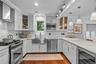 Kitchen featuring white cabinetry, light-toned stone countertops, stainless steel apron-front sink, wood-finish flooring, and integrated stainless ste