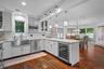 Kitchen featuring white cabinetry, stone-finish countertops, stainless steel farmhouse sink, built-in wine refrigerator, and wood-finish flooring
