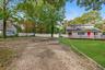 Expansive grounds featuring a wide gravel driveway, a manicured lawn with stone bordering, a wraparound deck with white railing, and a privacy fence