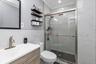 Bathroom featuring a wood-finish vanity with a rectangular sink, brushed nickel faucet, walk-in shower with sliding glass doors, dark tile shower floo