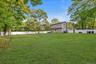 Expansive backyard featuring a large grass lawn, mature trees, and white vinyl privacy fencing