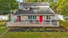 Multi-level residence featuring horizontal lap siding, stone veneer facade, a large elevated deck with white vinyl railing, dual red entry doors, and 
