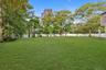 Expansive backyard featuring a level lawn, mature trees, and perimeter white vinyl fencing