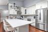 Kitchen featuring white shaker-style cabinetry, quartz countertops, stainless steel appliances, multi-toned tile backsplash, and wood-finish flooring