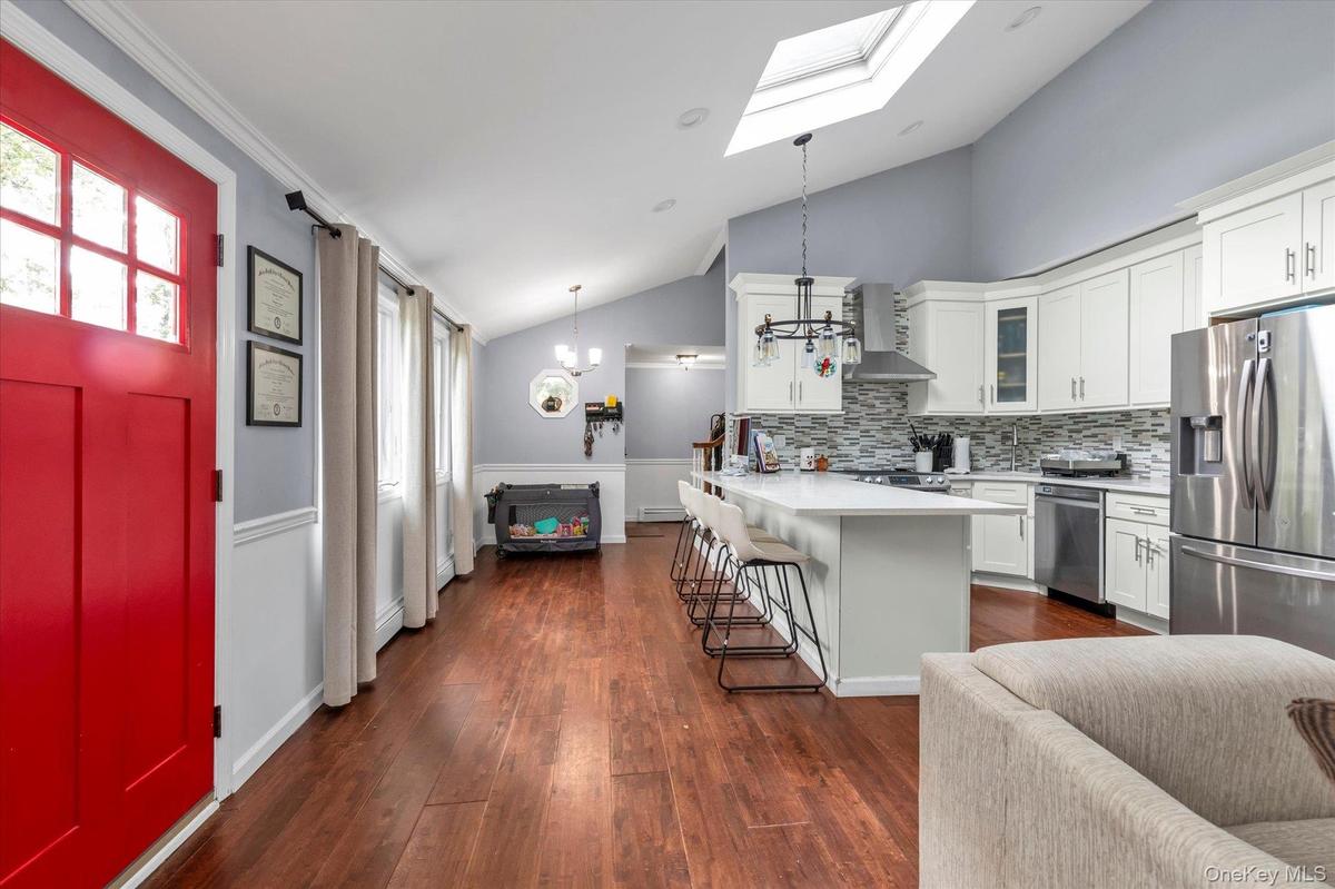 Vaulted ceilings with a skylight, wood-finish flooring, shaker-style cabinetry, solid-surface countertops, and a decorative tile backsplash