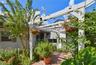 Charming landscaped front courtyard featuring a white pergola and a brick-paved walkway.