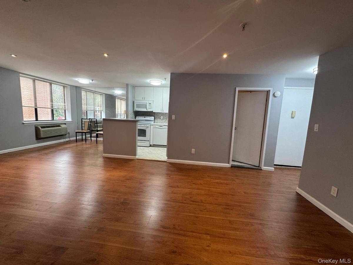 Open interior featuring wood-finish flooring, recessed lighting, white kitchen cabinetry, and large paneled windows