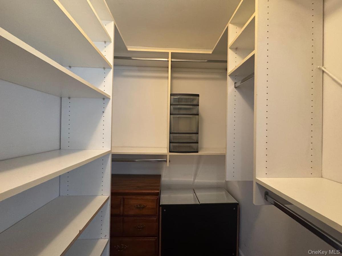 Walk-in closet featuring adjustable white shelving, dual-level hanging rods, and integrated cabinetry