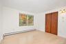 Light-toned wood-finish flooring, sliding wood-paneled closet doors, dual-pane window with exterior foliage scenery, and dual-light wall sconce