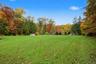 Expansive grassy lot featuring a perimeter of mature deciduous and evergreen trees