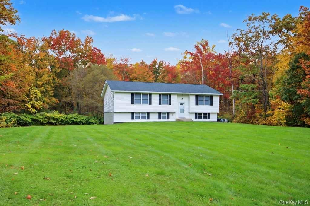 Split-level residence featuring white horizontal siding, dark-trimmed windows, a shingled roof, and an expansive lawn set against mature deciduous tre