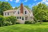Dutch Colonial exterior featuring shingle siding, a prominent brick chimney, arched windows, and manicured landscaping
