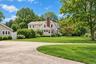 Gambrel-style exterior featuring a brick chimney, shingle siding, a sprawling lawn, and a circular gravel driveway with stone edging