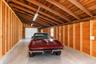 Spacious garage featuring exposed wood-stud walls, wood-paneled ceiling, concrete flooring, linear fluorescent lighting, and a white paneled garage do