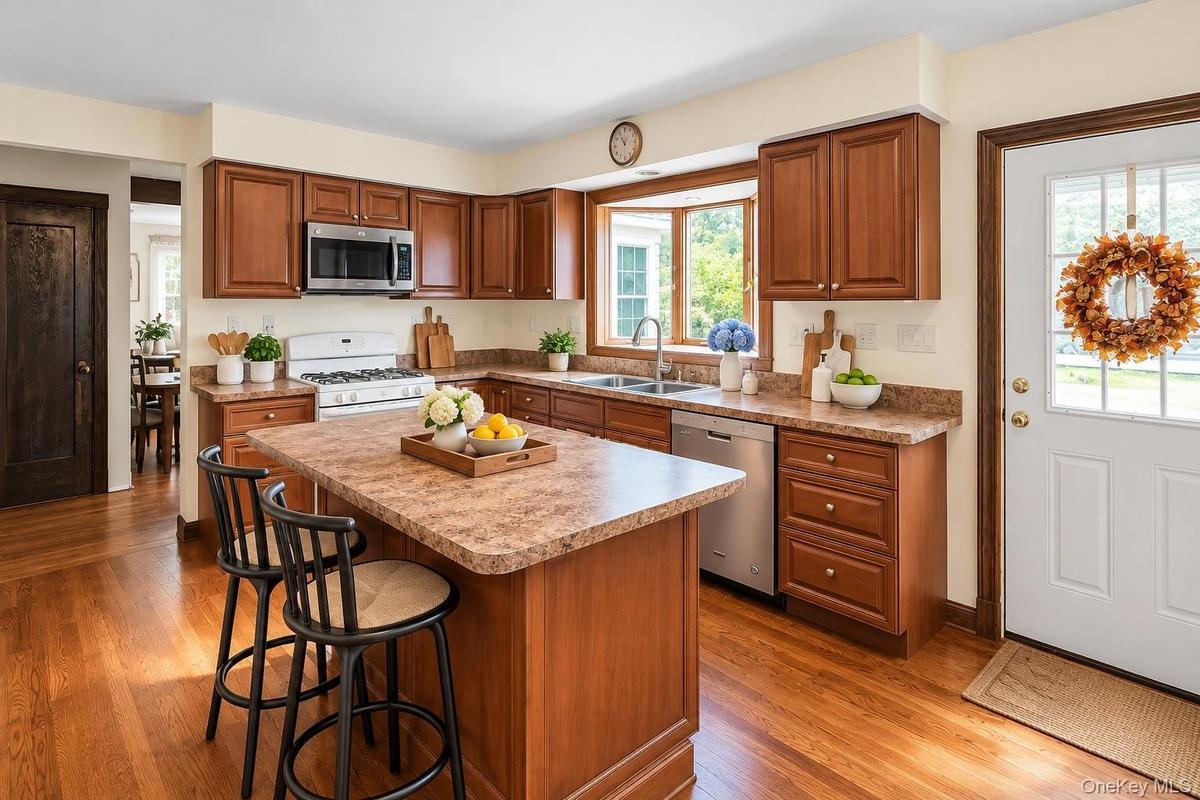 Kitchen featuring stained wood cabinetry, central island, laminate countertops, stainless steel appliances, and wood-finish flooring