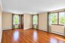 Interior room featuring wood-finish flooring, white walls, multiple windows with wooden frames, and a solid wood interior door
