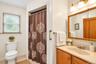 Bathroom featuring a wood-toned vanity with an integrated basin, triple-light wall-mounted fixture, medicine cabinet, and a shower area with a grab ba