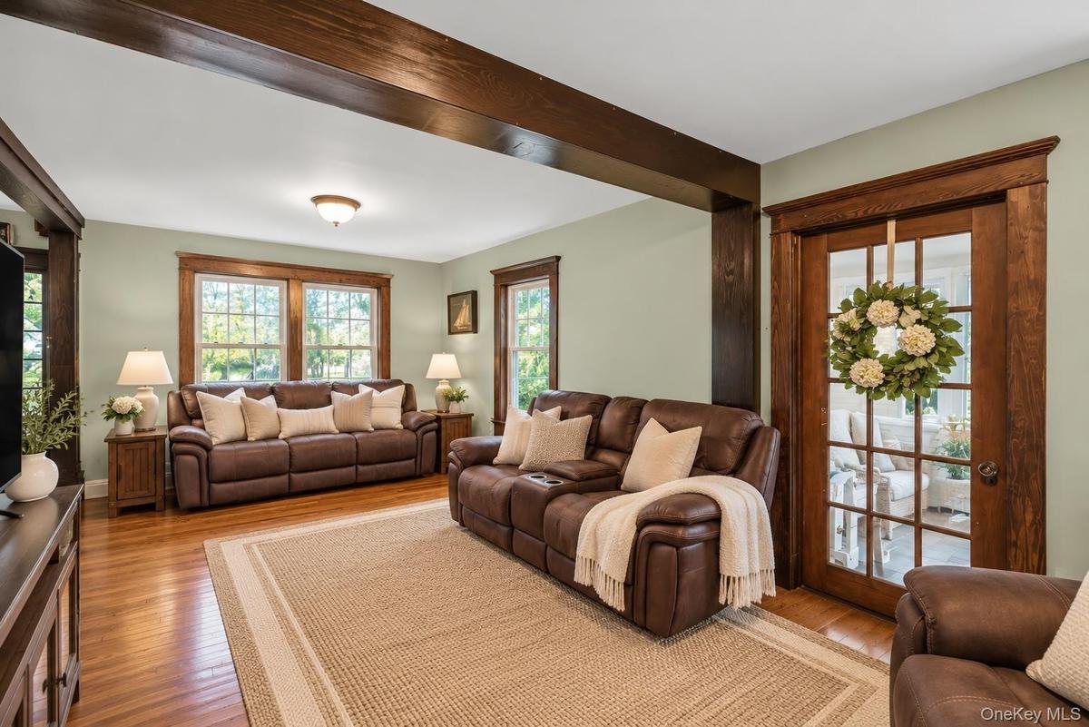 Living area featuring exposed wooden ceiling beams, natural wood-finish flooring, multi-pane windows with wooden trim, and a glass-paneled wooden door
