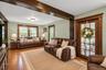 Living area featuring exposed wooden ceiling beams, natural wood-finish flooring, multi-pane windows with wooden trim, and a glass-paneled wooden door